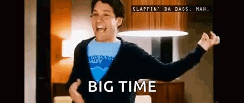 A Man In A Blue Shirt Is Dancing In A Living Room With The Words Big Time Written On The Bottom . GIF
