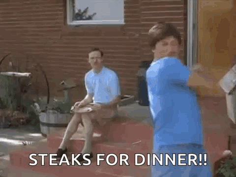A Man In A Blue Shirt Is Dancing In Front Of A Brick Building While Another Man Sits On The Steps . GIF