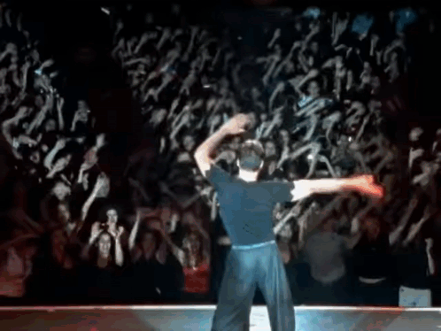 A Man In A Blue Shirt Is Dancing In Front Of A Crowd Of People . GIF
