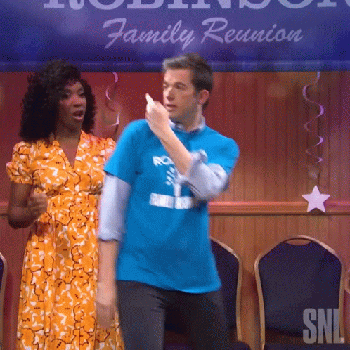 A Man In A Blue Shirt Is Dancing With A Woman In An Orange Dress In Front Of A Sign That Says Family Reunion GIF