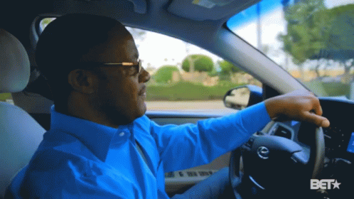 A Man In A Blue Shirt Is Driving A Car With A Bet Logo In The Corner GIF