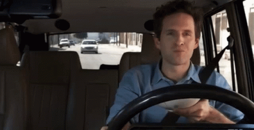 A Man In A Blue Shirt Is Driving A Car With A Bowl In His Hand GIF