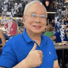 A Man In A Blue Shirt Is Giving A Thumbs Up Sign . GIF
