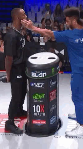 A Man In A Blue Shirt Is Giving Another Man A High Five In Front Of A Trash Can . GIF