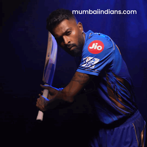 A Man In A Blue Shirt Is Holding A Bat And The Website Mumbaiindians.com Is Visible Behind Him GIF