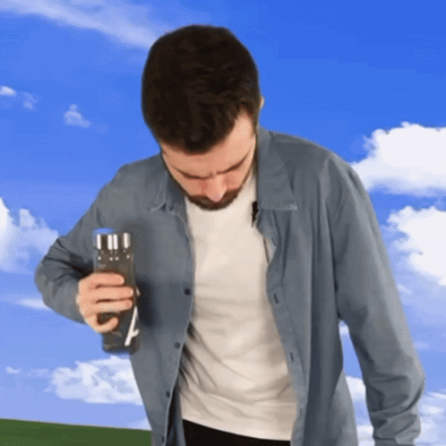 A Man In A Blue Shirt Is Holding A Bottle Of Water GIF