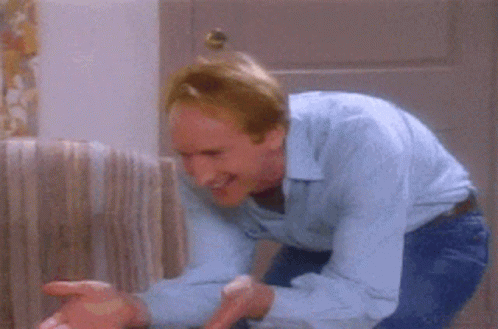 A Man In A Blue Shirt Is Holding A Cat In His Arms In A Living Room GIF