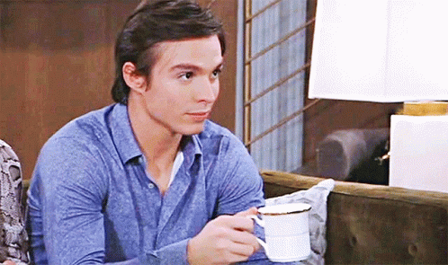 A Man In A Blue Shirt Is Holding A Cup Of Coffee . GIF