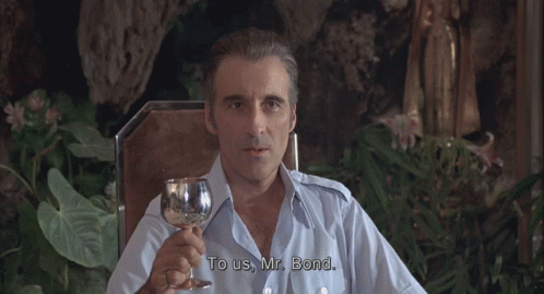 A Man In A Blue Shirt Is Holding A Glass Of Wine GIF