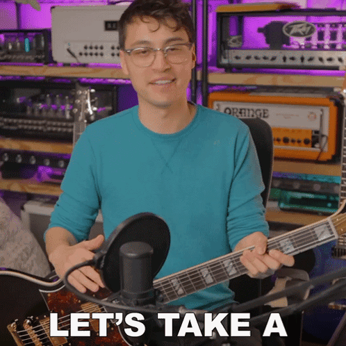A Man In A Blue Shirt Is Holding A Guitar In Front Of A Microphone With The Words Let 'S Take A Below Him GIF