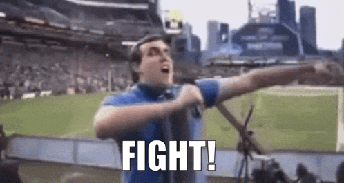 A Man In A Blue Shirt Is Holding A Microphone In A Stadium And Saying `` Fight '' . GIF