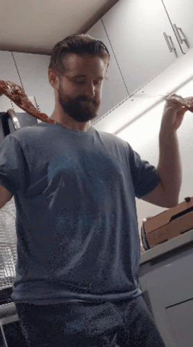 A Man In A Blue Shirt Is Holding A Slice Of Pizza In His Hand GIF