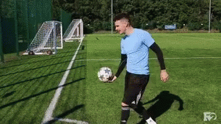 A Man In A Blue Shirt Is Holding A Soccer Ball On A Field . GIF