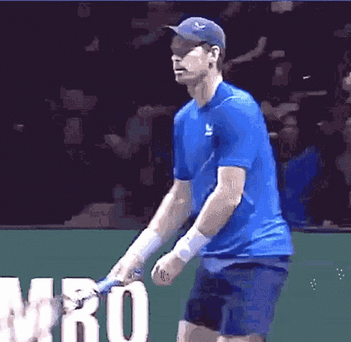 A Man In A Blue Shirt Is Holding A Tennis Racquet In Front Of The Word Mro GIF
