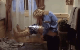 A Man In A Blue Shirt Is Holding A Woman 'S Leg In A Room . GIF