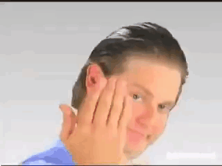 A Man In A Blue Shirt Is Holding His Hand To His Face And Smiling . GIF