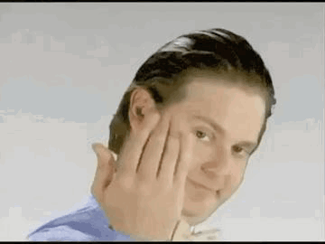 A Man In A Blue Shirt Is Holding His Hand To His Face . GIF