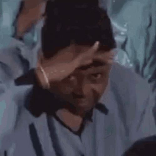 A Man In A Blue Shirt Is Holding His Hand To His Head . GIF