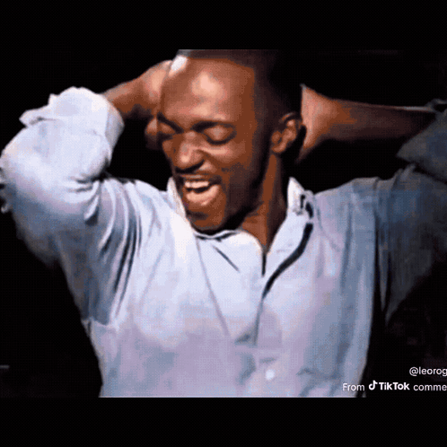 A Man In A Blue Shirt Is Holding His Head With His Hands . GIF