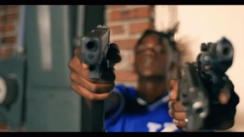 A Man In A Blue Shirt Is Holding Two Guns GIF