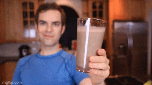 A Man In A Blue Shirt Is Holding Up A Glass Of Milk GIF