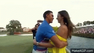 A Man In A Blue Shirt Is Hugging A Woman In A Yellow Dress On A Golf Course . GIF