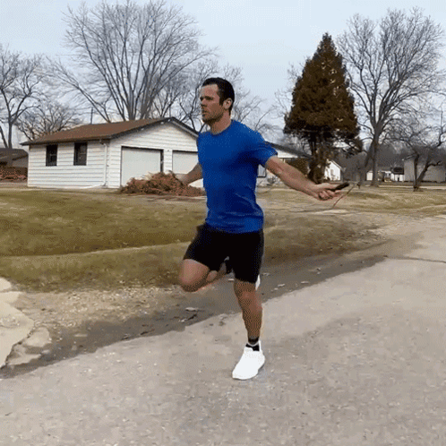 A Man In A Blue Shirt Is Jumping A Jump Rope On A Road GIF