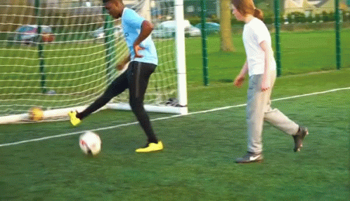 A Man In A Blue Shirt Is Kicking A Soccer Ball In Front Of A Goal GIF