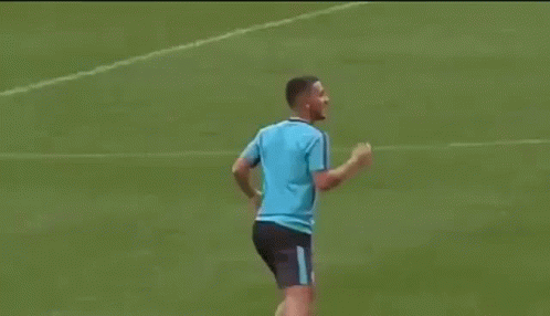 A Man In A Blue Shirt Is Kicking A Soccer Ball On A Soccer Field . GIF