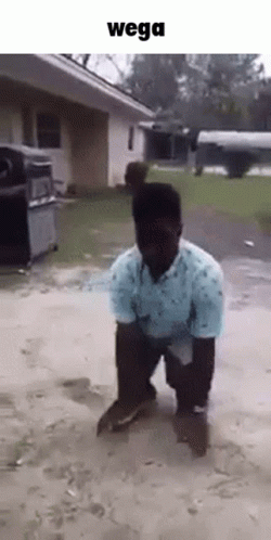 A Man In A Blue Shirt Is Kneeling On The Ground In Front Of A House With The Words Wega Above Him . GIF