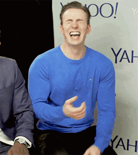 A Man In A Blue Shirt Is Laughing In Front Of A Wall That Says Yahoo GIF