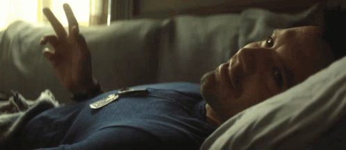 A Man In A Blue Shirt Is Laying In Bed With His Eyes Closed GIF