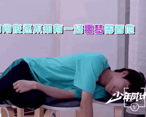 A Man In A Blue Shirt Is Laying On A Stool With Chinese Writing On It GIF