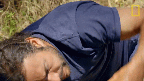 A Man In A Blue Shirt Is Laying On The Ground With A National Geographic Logo In The Background GIF