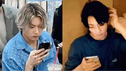 a man in a blue shirt is looking at a cell phone next to a man in a black shirt .