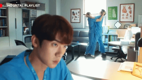 A Man In A Blue Shirt Is Looking At Another Man In A Hospital Playlist Room GIF
