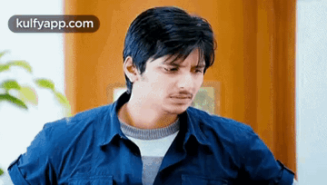A Man In A Blue Shirt Is Looking At The Camera . GIF