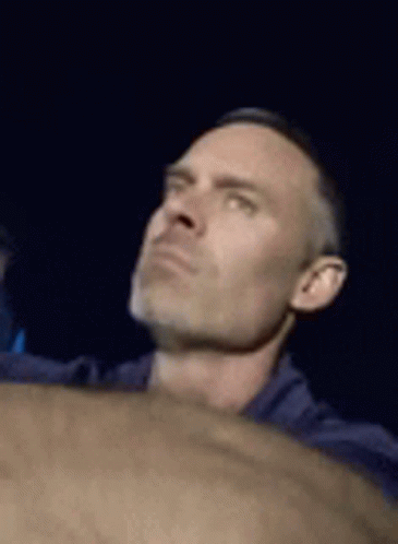 A Man In A Blue Shirt Is Looking Up At Something In The Dark . GIF