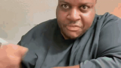 A Man In A Blue Shirt Is Making A Funny Face And Pointing At The Camera . GIF