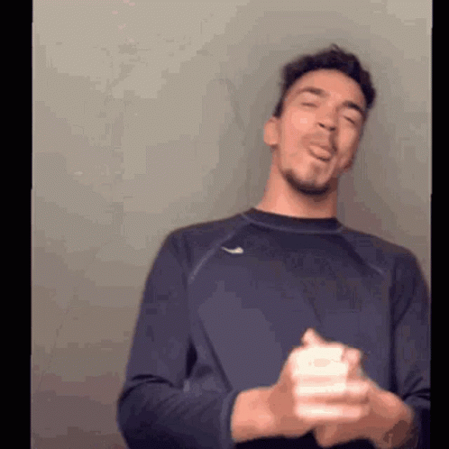 A Man In A Blue Shirt Is Making A Funny Face While Holding A White Object In His Hands . GIF