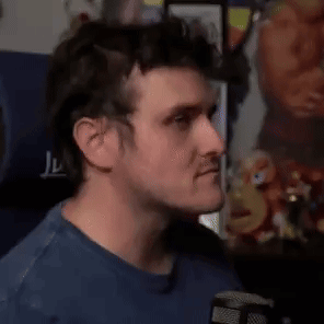 A Man In A Blue Shirt Is Making A Funny Face While Holding His Finger To His Lips . GIF
