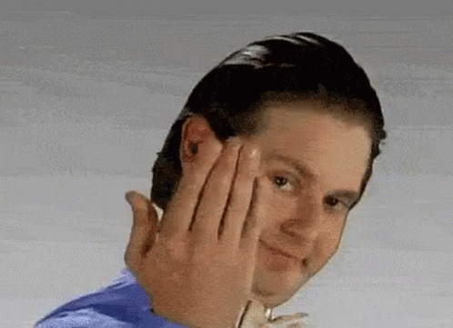 A Man In A Blue Shirt Is Making A Funny Face With His Hands . GIF