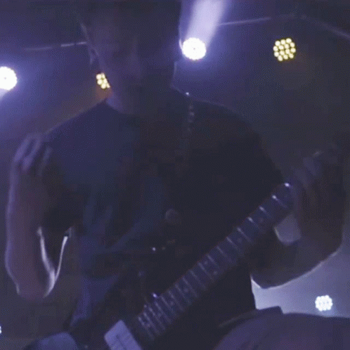 a man in a blue shirt is playing a guitar with the letters h and i on the neck