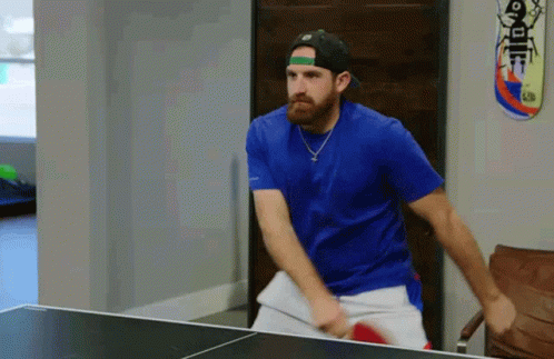 A Man In A Blue Shirt Is Playing Ping Pong With A Skateboard On The Wall GIF