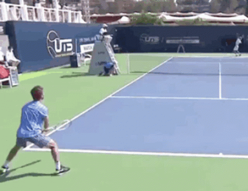 A Man In A Blue Shirt Is Playing Tennis On A Court With A U15 Sign In The Background GIF
