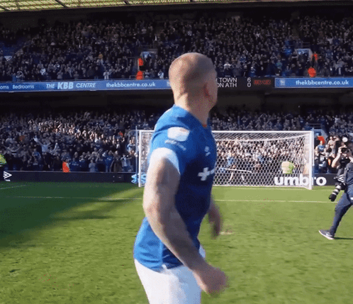 a man in a blue shirt is running on a soccer field in front of a sign that says umbro