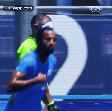 A Man In A Blue Shirt Is Running On A Track With A Man In A Green Shirt Behind Him . GIF