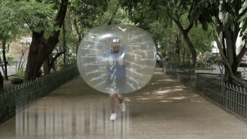 A Man In A Blue Shirt Is Running Through A Clear Bubble On A Sidewalk GIF