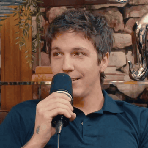 a man in a blue shirt is singing into a microphone with a tattoo on his wrist