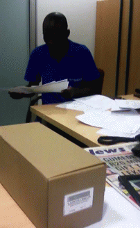 A Man In A Blue Shirt Is Sitting At A Desk With A Box That Says News GIF